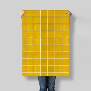 Peut inclure: Une grande feuille rectangulaire de carreaux jaunes avec des lignes de jointoiement blanches est tenue. Les carreaux sont d'une couleur jaune doré chaud, et les lignes de jointoiement créent un motif en grille. La feuille est tenue sur un fond gris uni.