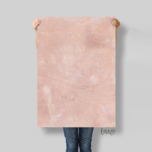 May include: A large, pink, textured poster with a distressed, vintage look. The poster is being held up by a person's hands.