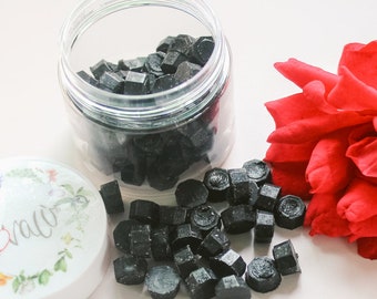 May include: A clear plastic jar filled with black wax seal beads. The jar sits next to a lid with floral accents and the word "Grace" in script. A vibrant red rose is also in the image.