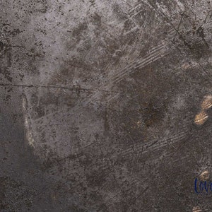 May include: A close-up of a dark gray textured surface with scratches and marks. The surface has a metallic sheen and appears to be made of metal.