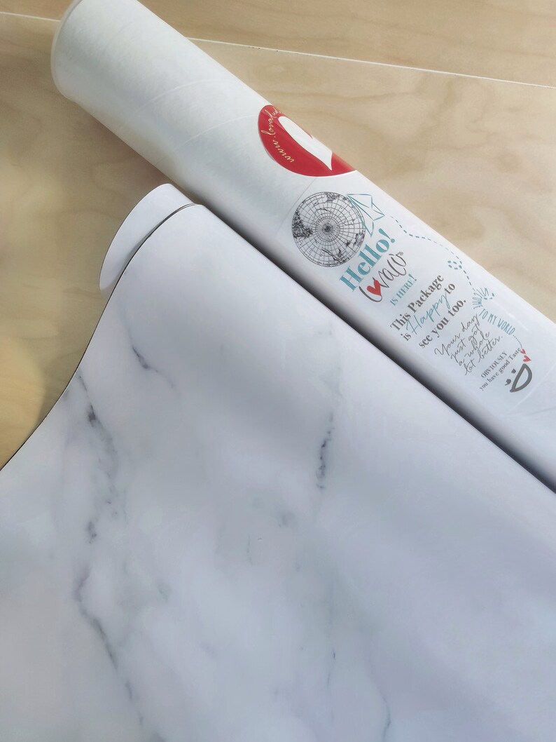 May include: A white tube with a red heart and the text "Hello! Walo" on it. The tube is rolled up and the text "This Package is Happy to see you too." is visible. The tube is on a white marble surface.