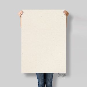 May include: A large, rectangular, off-white paper sheet held by a person. The paper has a textured surface with small flecks. The person is wearing blue jeans. The bottom right corner has the handwritten word "lovaco".