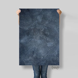 May include: A rectangular, dark blue textured art print. The print has a rough, mottled appearance with variations in tone. The print is held up by a person. The bottom right corner of the print has the word "lovaco" in a script font.