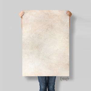 May include: A large rectangular backdrop with a textured, off-white and beige surface. The backdrop is held by a person wearing blue jeans. The bottom right corner has the handwritten word "Lovaco".