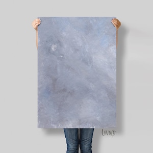 May include: An abstract rectangular painting with a textured, blended appearance in shades of grey and blue. The artwork is held up by a person, with the bottom half of their body visible. The painting has a soft, diffused aesthetic.