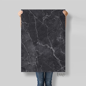 May include: A black and white marble-patterned poster with a subtle grey background. The poster is being held by a person's hands.