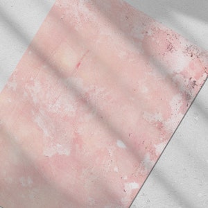 May include: A textured, pink surface with white and darker pink accents. The surface is angled, with a white background in the corner. Shadows from an unseen object cast diagonal lines across the pink surface.