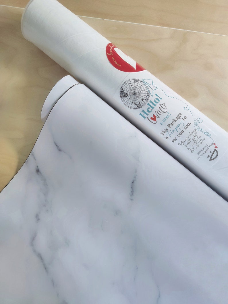 Pu&ograve; includere: Un tubo bianco con un cuore rosso e il testo "Hello! Walo" su di esso. Il tubo &egrave; arrotolato e il testo "This Package is Happy to see you too." &egrave; visibile. Il tubo &egrave; su una superficie di marmo bianco.