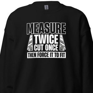 May include: Black sweatshirt with white text that reads "Measure Twice Cut Once Then Force It To Fit". The text is surrounded by two white images of a saw.