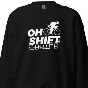 May include: Black sweatshirt with the text "OH SHIFT" in white, along with a white graphic of a cyclist on a bicycle. The sweatshirt is a crew neck style.