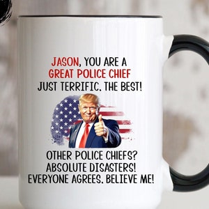 May include: White ceramic coffee mug with a black handle. The mug features a graphic of a man with a thumbs up gesture in front of an American flag. The text on the mug reads "JASON, YOU ARE A GREAT POLICE CHIEF JUST TERRIFIC. THE BEST! OTHER POLICE CHIEFS? ABSOLUTE DISASTERS! EVERYONE AGREES. BELIEVE ME!"