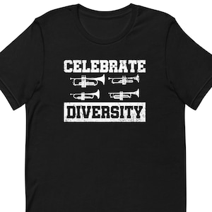 May include: Black t-shirt with a white graphic that reads "CELEBRATE DIVERSITY." The design includes four trumpet illustrations. The shirt is made of a soft material and has short sleeves.
