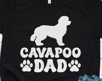 May include: Black t-shirt with a white silhouette of a Cavapoo dog and the text "Cavapoo Dad" with white paw prints on either side of the text.