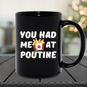 May include: Black ceramic coffee mug with a white graphic that says "You had me at poutine" with a cartoon image of a Canadian flag on a container of fries and gravy.