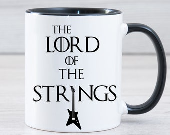 May include: White ceramic mug with a black rim and handle. The mug has a black graphic that says "The Lord of the Strings" with a black electric guitar graphic.