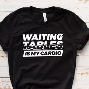 May include: Black t-shirt with white text that reads "WAITING TABLES IS MY CARDIO".