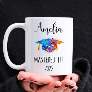 May include: White ceramic mug with a colorful graduation cap design and the text "Amelia Mastered It! 2022"