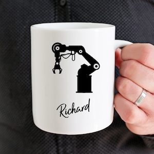 May include: White ceramic mug with a black silhouette of a robotic arm and the name "Richard" written in cursive.