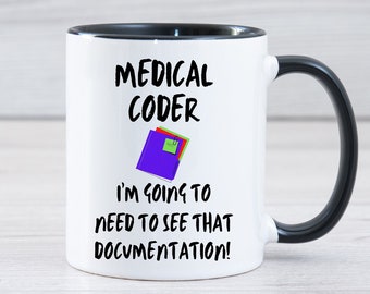 May include: White coffee mug with a black rim and handle. The mug has a black and white graphic that says "Medical Coder I'm going to need to see that documentation!" with a purple folder icon.
