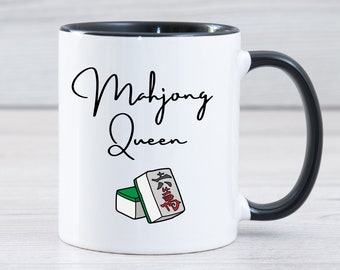 May include: White ceramic mug with a black rim and handle. The mug has the text "Mahjong Queen" in black cursive writing and a cartoon image of two mahjong tiles.