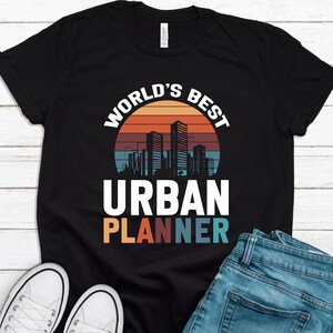 May include: Black t-shirt with a retro sunset graphic and the text "World's Best Urban Planner".