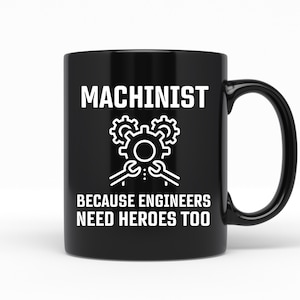 May include: Black coffee mug with white text that reads "Machinist because engineers need heroes too". The mug has a white image of gears and wrenches.