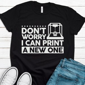 Może przedstawiać: Czarny T-shirt z białym nadrukiem przedstawiającym drukarkę 3D i tekstem "Nie martw się, mogę wydrukować nowy".