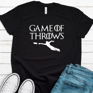 May include: Black t-shirt with white text that reads "Game of Throws" and a silhouette of a person throwing a frisbee.