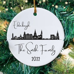 May include: White ceramic Christmas ornament with a black silhouette of the Edinburgh skyline and the text "Edinburgh" at the top, "The Smith Family" in the middle, and "2022" at the bottom.