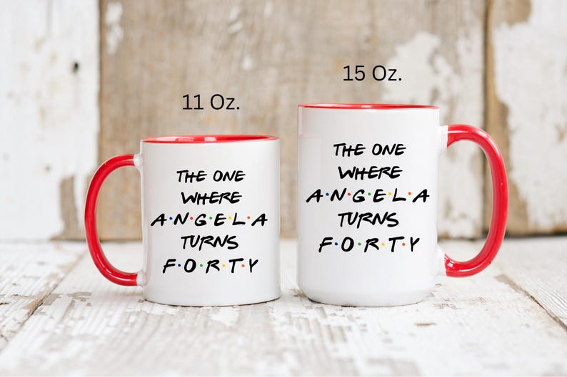 Op de afbeelding: Twee witte keramische mokken met rode binnenkant en handvatten. De mokken hebben de tekst "THE ONE WHERE ANGELA TURNS FORTY" in het zwart. E&eacute;n mok is 312 ml, de andere 425 ml.