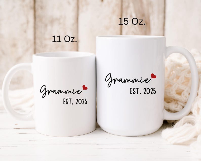 May include: Two white ceramic mugs with black text that reads "Grammy Est. 2025" and a small red heart. The mug on the left is 11 oz and the mug on the right is 15 oz.