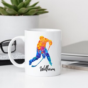 May include: White ceramic coffee mug with a colorful watercolor illustration of a hockey player and the name "William" printed on the bottom.