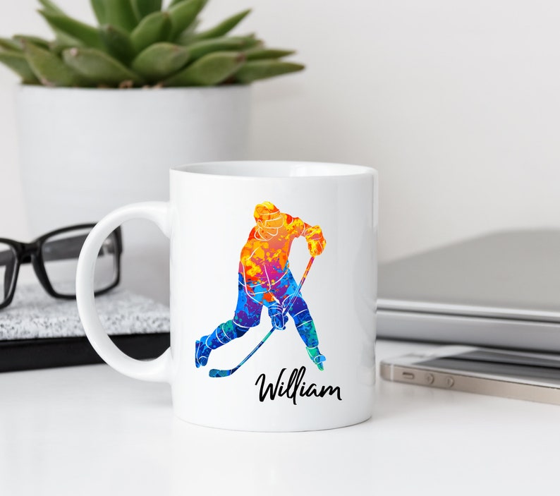 May include: White ceramic coffee mug with a colorful watercolor illustration of a hockey player and the name "William" printed on the bottom.