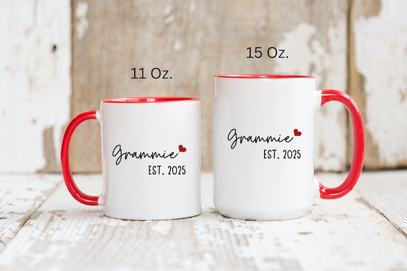 May include: Two white ceramic mugs with red rims and handles. The smaller mug is 11 ounces and the larger mug is 15 ounces. Both mugs have the text "Grammy Est. 2025" with a small red heart.