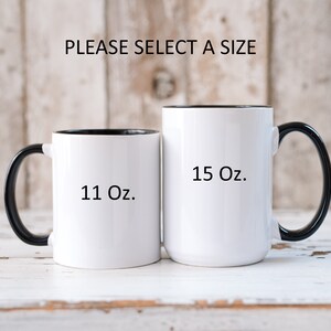 May include: Two white ceramic mugs with black handles and black rims. The mug on the left is 11 oz and the mug on the right is 15 oz.