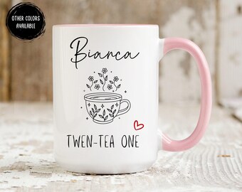May include: White ceramic mug with a pink handle and rim. The mug features the name "Bianca" in script, a floral teacup illustration, and the phrase "TWEN-TEA ONE" in black text. A small red heart is also present.