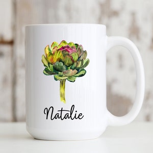 May include: White ceramic mug with a watercolor illustration of an artichoke in shades of green, yellow, and purple. The name "Natalie" is written in black cursive below the artichoke.