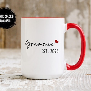 May include: White ceramic mug with a red rim and handle. The mug has black text that reads "Grammy Est. 2025" with a small red heart.
