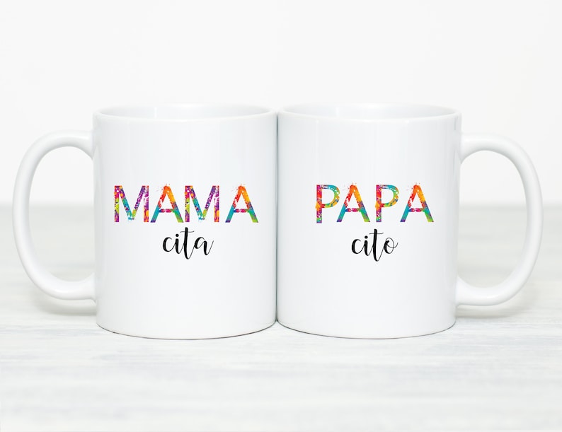 May include: Two white ceramic mugs with colorful text. The mug on the left says "MAMA cita" and the mug on the right says "PAPA cito".