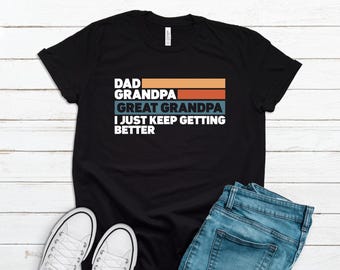 May include: Black t-shirt with a retro-style design that says "Dad Grandpa Great Grandpa I Just Keep Getting Better".