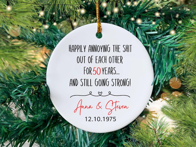 May include: White round Christmas ornament with black text that reads "Happily annoying the shit out of each other for 50 years... and still going strong!" with the names "Anna & Steven" and the date "12.10.1975" in red.