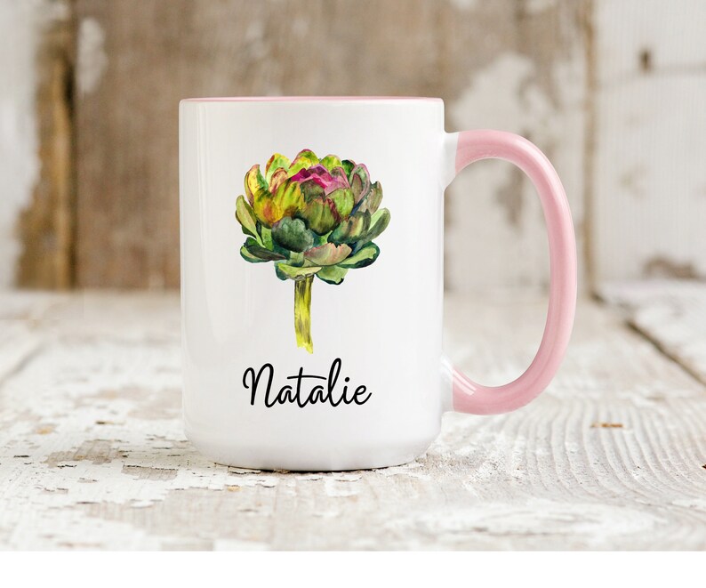 May include: White ceramic mug with a pink handle. The mug features a watercolor illustration of an artichoke and the name "Natalie" printed in black.