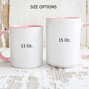 May include: Two white ceramic mugs with pink rims and handles. The mug on the left is 11 oz and the mug on the right is 15 oz.