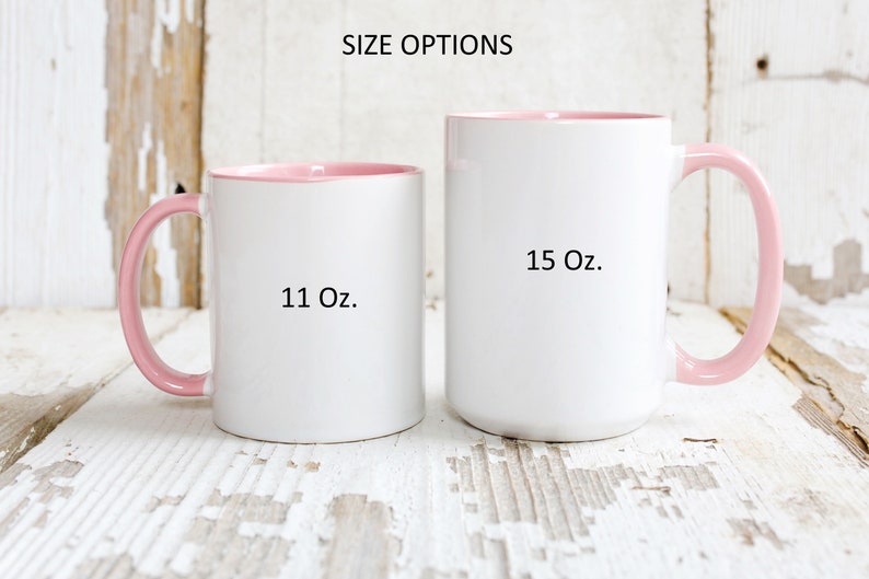 May include: Two white ceramic mugs with pink rims and handles. The mug on the left is 11 oz and the mug on the right is 15 oz.