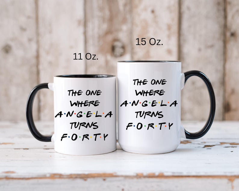 Op de afbeelding: Twee witte keramische mokken met zwarte handvatten en randen. De mokken hebben de tekst "THE ONE WHERE ANGELA TURNS FORTY" in zwart, met het woord "FORTY" in kleurrijke letters. E&eacute;n mok is 312 ml, de andere 425 ml.