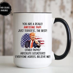 May include: White ceramic mug with a black handle and rim. The mug features text that reads "YOU ARE A REALLY AWESOME PAPI" and an image of a man with an American flag background.