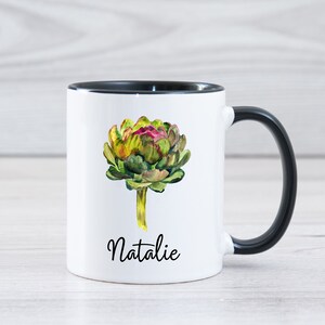 May include: White ceramic mug with a black rim and handle. The mug features a watercolor illustration of an artichoke with the name "Natalie" printed below.