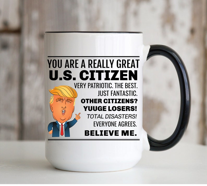 K&ouml;nnte beinhalten: Eine wei&szlig;e Keramik-Kaffeetasse mit schwarzem Rand und Henkel. Die Tasse zeigt eine Schwarzwei&szlig;illustration eines Mannes mit roter Krawatte und dem Text "YOU ARE A REALLY GREAT U.S. CITIZEN VERY PATRIOTIC. THE BEST. JUST FANTASTIC. OTHER CITIZENS? YUUGE LOSERS! TOTAL DISASTERS! EVERYONE AGREES. BELIEVE ME."
