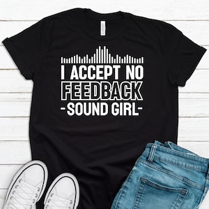 May include: Black t-shirt with the text "I ACCEPT NO FEEDBACK - SOUND GIRL" in white. The shirt features a sound wave graphic above the text. White sneakers and blue jeans are visible in the image.