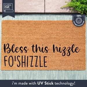 Könnte beinhalten: Eine braune Kokosfaser-Fußmatte mit dem Text "Bless this hizzle FO'SHIZZLE" in schwarzer kursivschrift. Die Fußmatte hat ein 100% Kundenzufriedenheits-Garantieetikett in der oberen rechten Ecke. Die Fußmatte ist mit UV Stick-Technologie hergestellt.